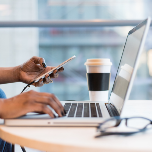 A pair of hands working on a laptop and using a cell phone